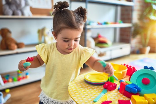 Beautiful toddler playing on the table with plastic vegetables and dishes at kindergarten