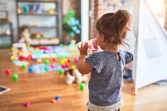 Beautiful toddler standing drinking milk sucking baby bottle at kindergarten