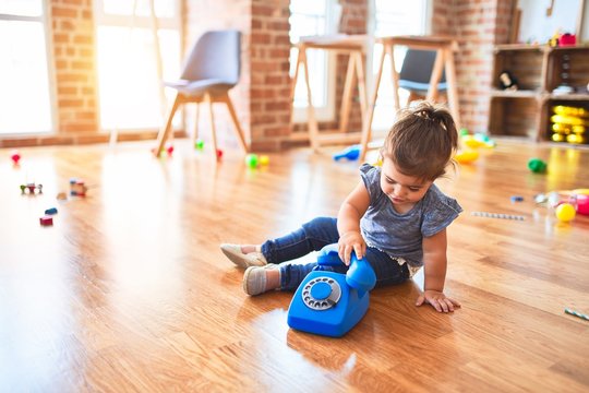 Beautiful toddler sitting on the floor playing with vintage phone at kindergarten