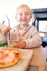 Beautiful toddler child girl sitting on baby highchair drinking juice using straw with happy face