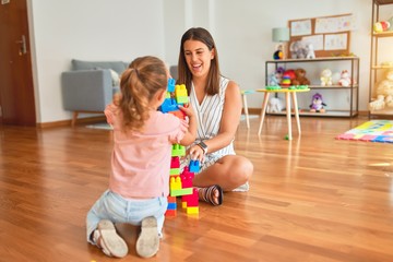 Beautiful teacher and blond toddler girl building tower using plastic blocks at kindergarten