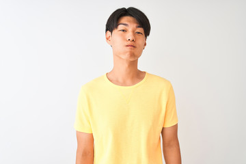 Chinese man wearing yellow casual t-shirt standing over isolated white background puffing cheeks with funny face. Mouth inflated with air, crazy expression.