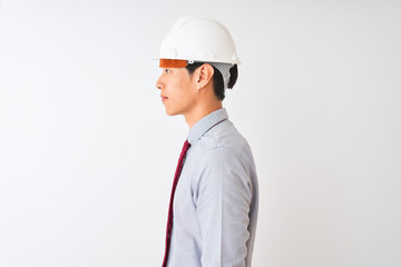 Chinese architect man wearing tie and helmet standing over isolated white background looking to side, relax profile pose with natural face with confident smile.