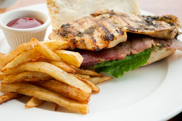  Sandwich prepared with grilled chicken with roast beef, french fries and tomato sauce, served outdoors on wooden table in Guatemala.