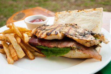  Sandwich prepared with grilled chicken with roast beef, french fries and tomato sauce, served outdoors on wooden table in Guatemala.