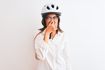 Beautiful businesswoman wearing glasses and bike helmet over isolated white background smelling something stinky and disgusting, intolerable smell, holding breath with fingers on nose. Bad smells 