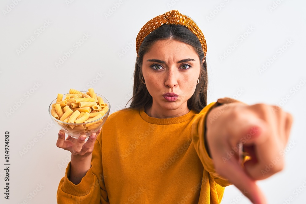 Poster Young beautiful woman holding bowl with macaroni pasta over isolated white background pointing with finger to the camera and to you, hand sign, positive and confident gesture from the front - Posters
