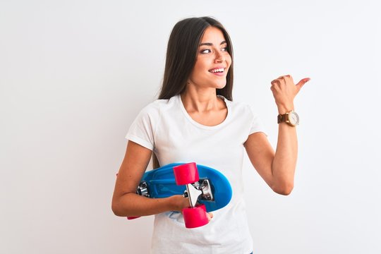 Young beautiful woman holding skate standing over isolated white background pointing and showing with thumb up to the side with happy face smiling