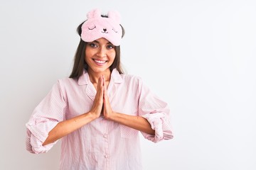 Young beautiful woman wearing sleep mask and pajama over isolated white background praying with hands together asking for forgiveness smiling confident.