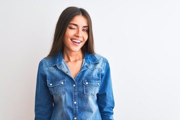 Obraz premium Young beautiful woman wearing casual denim shirt standing over isolated white background winking looking at the camera with sexy expression, cheerful and happy face.