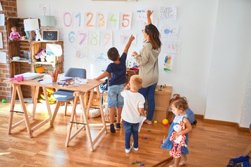 Fototapeta premium Beautiful teacher and group of toddlers playing around lots of toys at kindergarten
