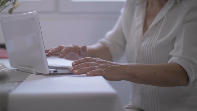 Senior woman is typing on laptop at home