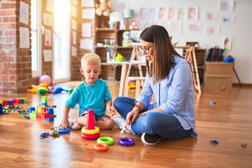 Young caucasian child playing at playschool with teacher. Mother and son at playroom with intelligence toy