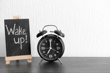 Alarm clock and chalkboard with text WAKE UP on table