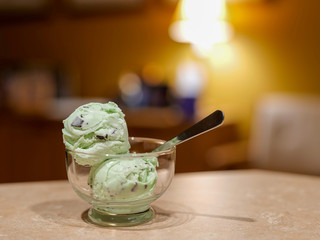Ice cream and spoon in glass dish on table with blurred background. Two scoops of delicious mint chocolate chip for dessert.