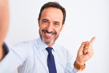 Middle age businessman wearing tie make selfie standing over isolated white background very happy pointing with hand and finger to the side