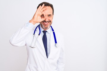 Middle age doctor man wearing coat and stethoscope standing over isolated white background doing ok gesture with hand smiling, eye looking through fingers with happy face.