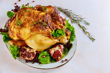 Traditional whole roasted chicken on plate with pomegranate, rosemary and green salad.