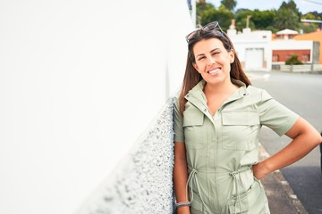 Beautiful girl leaning on white wall, young friendly woman smiling happy on a sunny day of summer