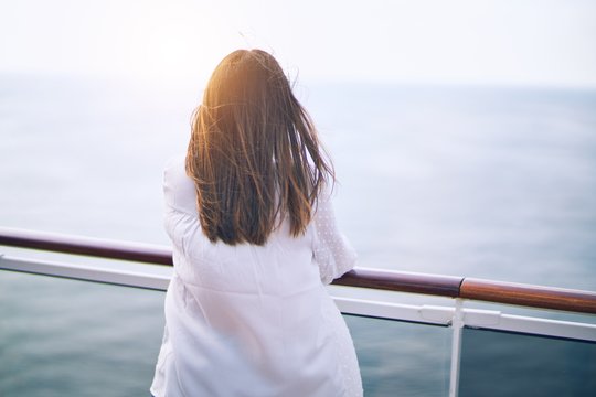 Young beautiful woman on vacation standing on a deck of ship with smile on face backwards doing a cruise