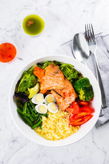 Healthy meal, keto food concept. Fish salad bowl on marble table background. Salad with salmon, couscous, vegetables, quail eggs. Top view, copy space