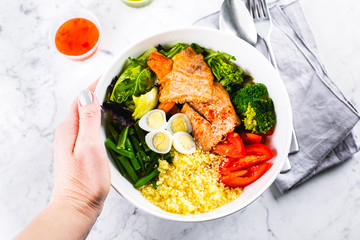Healthy meal, keto food concept. Fish salad bowl on marble table background. Salad with salmon, couscous, vegetables, quail eggs. Top view, copy space