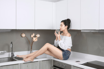 Sexy Asian woman talking by mobile phone while sitting in the kitchen.