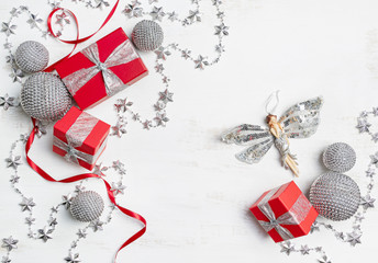 Christmas gifts on on a rustic white background. Xmas decorations such as twinkling silver stars, shiny silver baubles and a glowing silver angel surround bright red presents with silver ribbon.