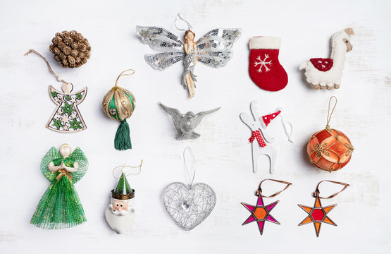 Vintage Christmas decorations / ornaments photographed from above on a white wooden rustic background. Include bauble, santa claus, reindeer, angle, stocking, lama, pine cone, bird, stars and heart.  