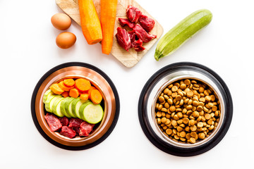 Pet feed ingredients. Raw meat and fresh vegetables near bowl with dry feed on white background top-down