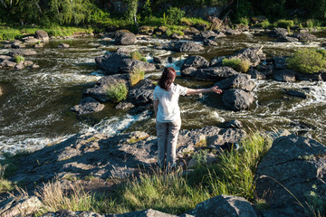 girl in a white shirt on the background of a fast mountain river running among