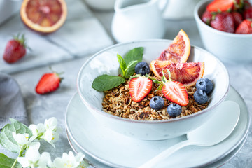 Healthy breakfast with granola, yogurt, fruits, berries on a white plate in white plate.