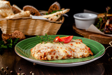 The concept of Italian cuisine. Baked lasagna with minced bolognese, pasta, cherry tomatoes lies on a green plate in a restaurant. A glass of red wine and bread basket on the table