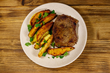 Fried beef steak with potato wedges on wooden table. Top view