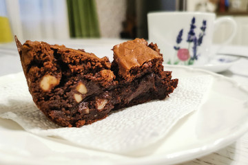 Chocolate brownie dessert on a white saucer, with a mug in the background. The concept of a cozy...