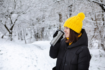 smiling woman in winter outfit drinking warm up drink from refillable mug