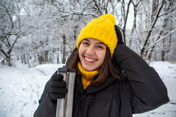 smiling woman in winter outfit drinking warm up drink from refillable mug