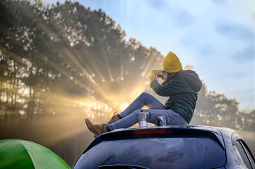 Woman traveller enjoy coffee time and make selfie on her owns roof of the car with scenery view of the mountain and mist morning in background