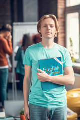 Blonde student wearing jeans and blue t-shirt holding English book