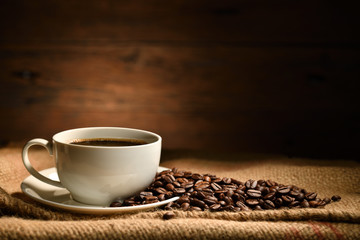 Cup of coffee and coffee beans on burlap sack on old wooden background
