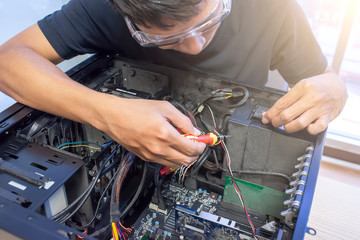 Male motherboard repairer using a screwdriver to replace the motherboard Concept of computer repair, close-up view of hardware - selective focus