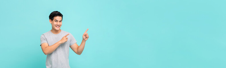 Cheerful smiling young Asian man pointing hands to copy space aside