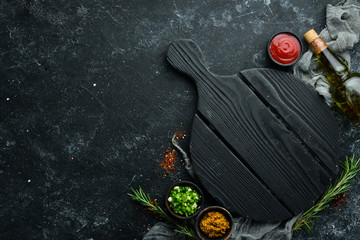 Kitchen board and vegetables with spices on black stone background. Top view. Free space for your text.