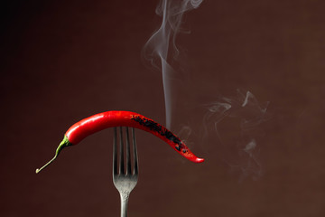 Hot chili red pepper smoking on a fork. Spice concept.