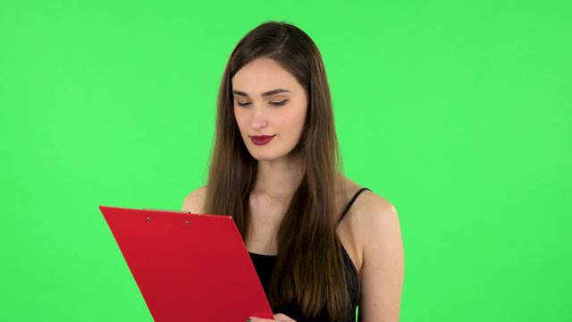 Woman fills papers in red folder with pen. Green screen