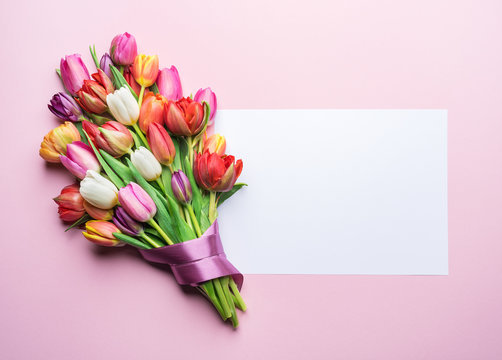 Colorful bouquet of tulips and a paper on pink background.