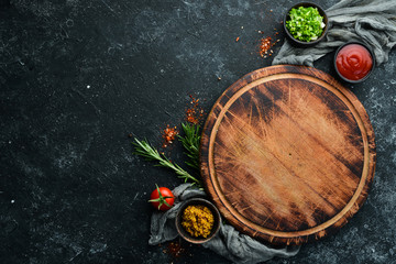 Kitchen board and vegetables with spices on black stone background. Top view. Free space for your text.