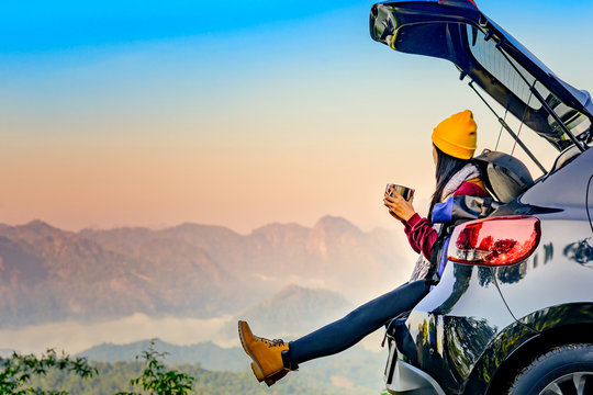 Woman traveller enjoy coffee time on back storage of car with scenery view of the mountain and mist morning in background