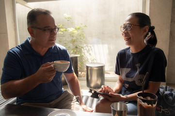 Happy senior American man and Asian woman couple drinking coffee  in coffeeshop