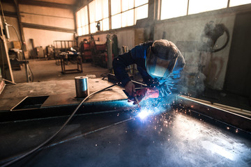 Professional welder welding metal construction parts in industrial workshop. An experienced worker...